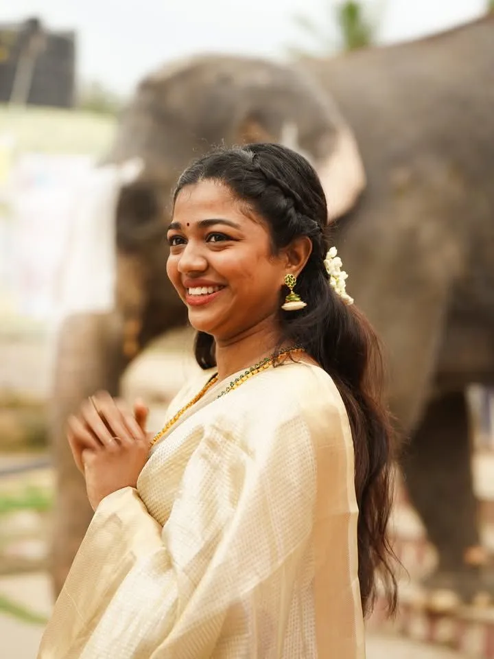 Amala Shaji in a Kasavu saree standing near an elephant