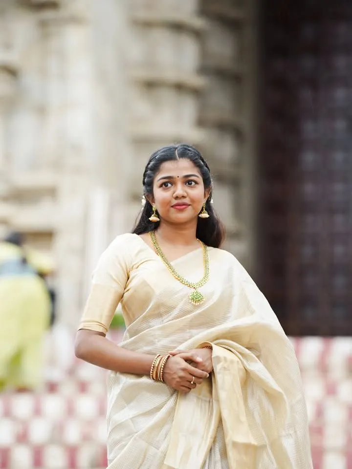 Amala Shaji in an Onam saree standing near historical place