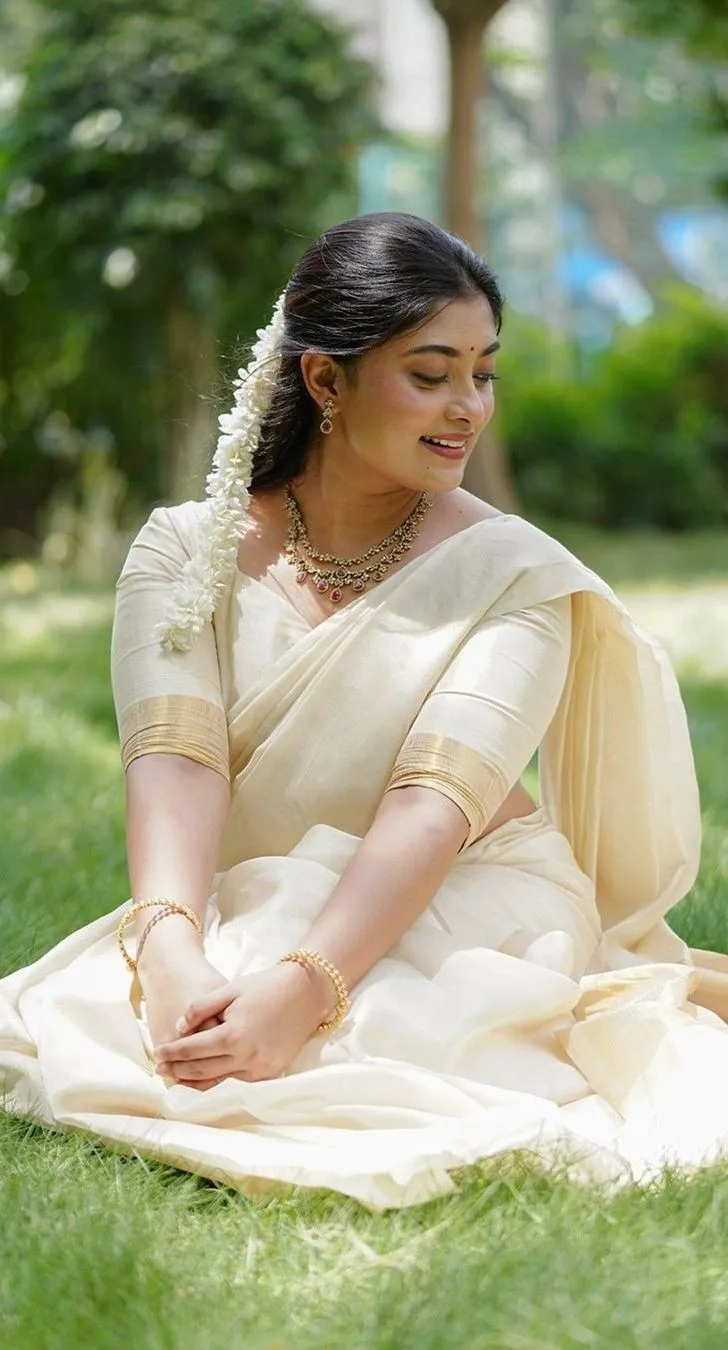 Ammu Abhirami in a neriyal saree sitting in the grass image