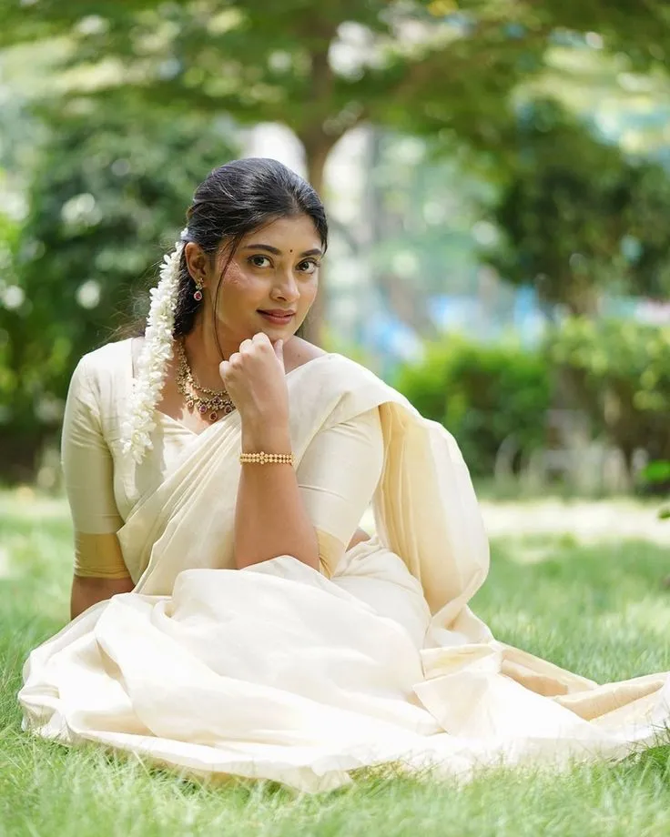 Ammu Abhirami in a Neriyal saree sitting in the grassy field