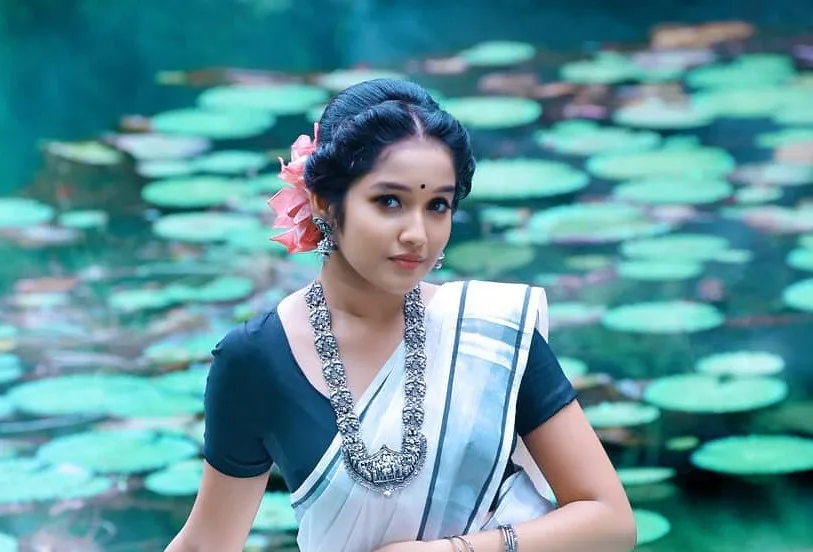 Anikha Surendran in a traditional saree sitting near a pond