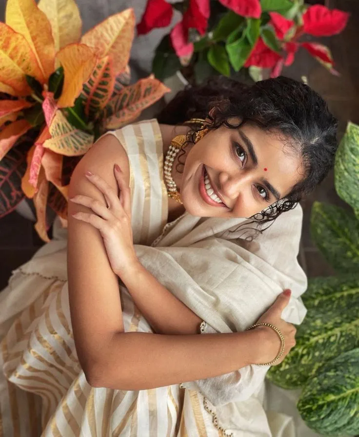 Anupama Parameswaran sitting near green plants wearing saree