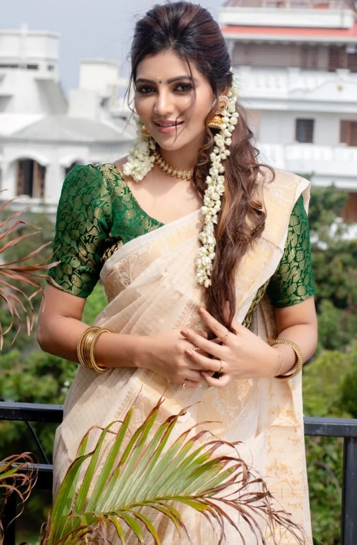 Athulya Ravi in an Onam saree standing near a black fence