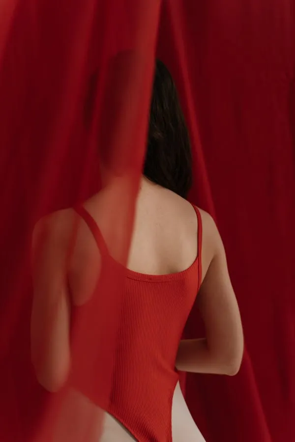 Back View of a Woman in a Red Dress Standing with a Curtain
