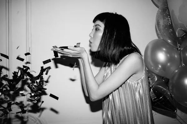 Black and White Photo of a Woman Blowing Confetti At a Party