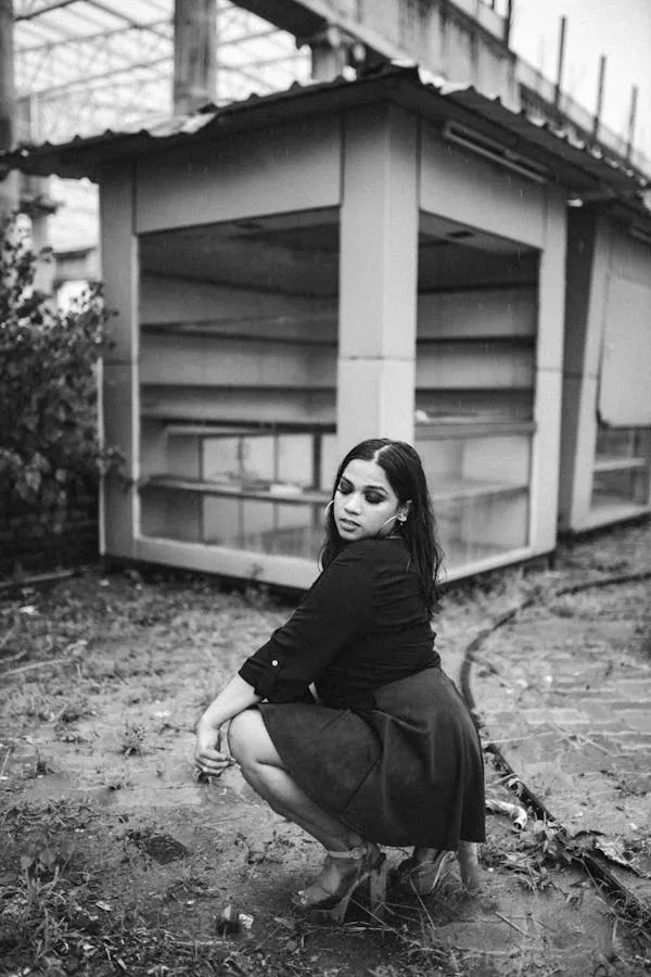 Black and White Photo of a Woman Crouching Near a Structure