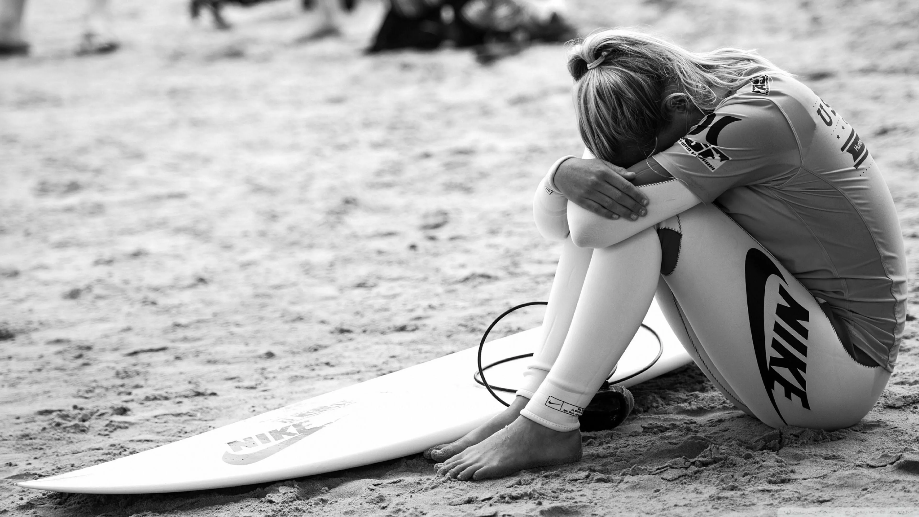 Black and White Photo of a Woman Resting by a Surfboard