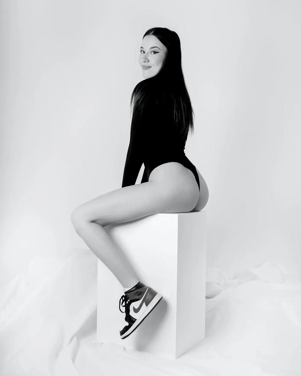 Black and White Photo of a Woman Sitting on a White Cube