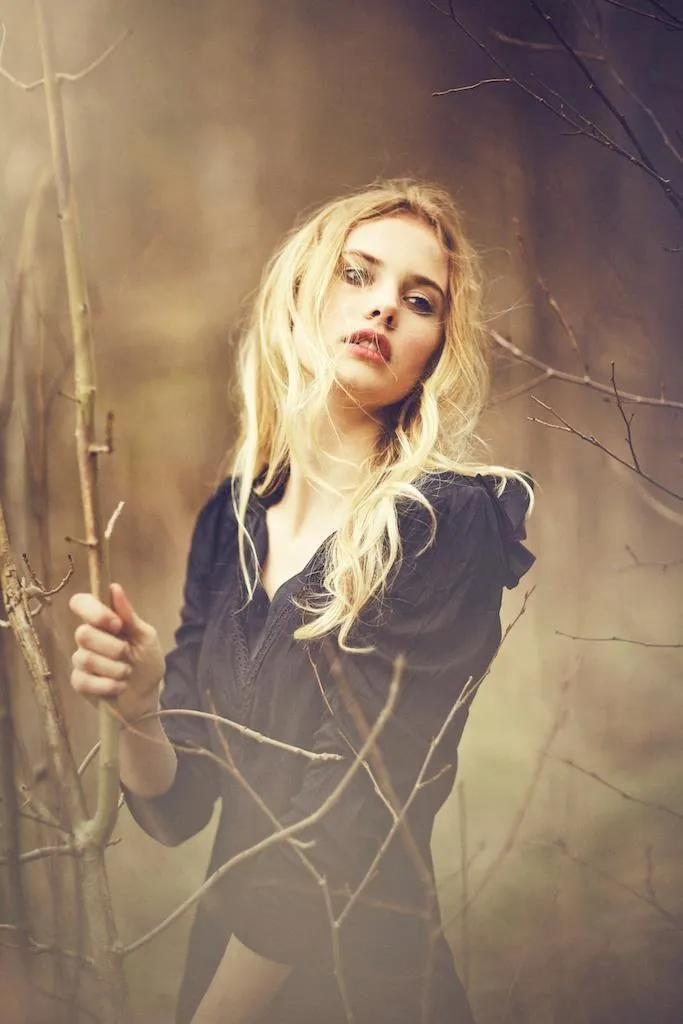 Blonde Woman Standing Outdoors with Branches in the Backdrop