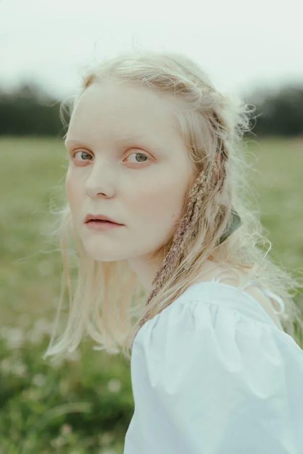 Blonde Woman in a White Dress Standing in a Green Field