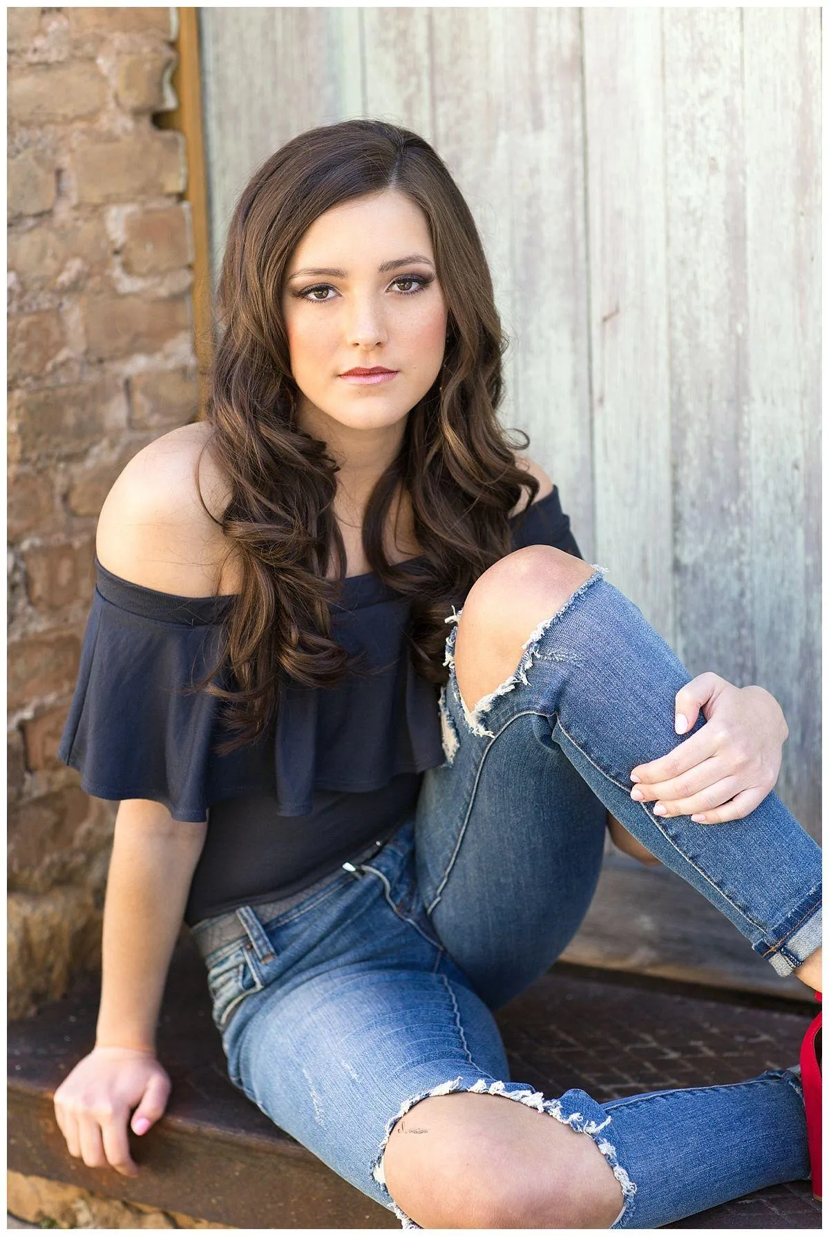 Casual Girl in Ripped Jeans Sitting Against a Rustic Wall
