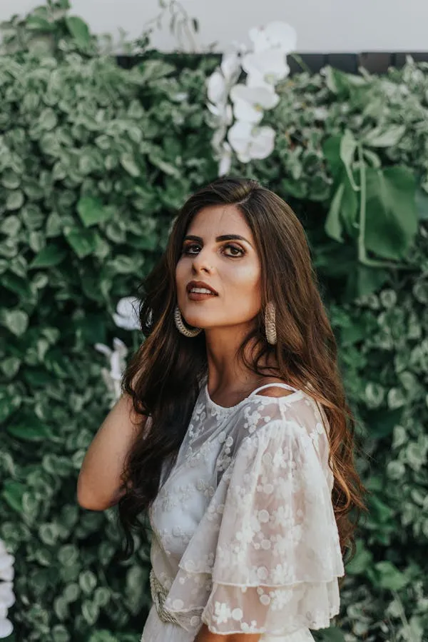 Classy Woman in a White Lace Top Standing Near Green Leaves