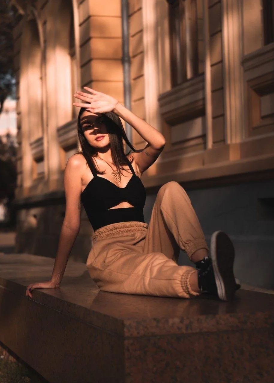 Confident Woman in a Black Top Sitting Near a City Building