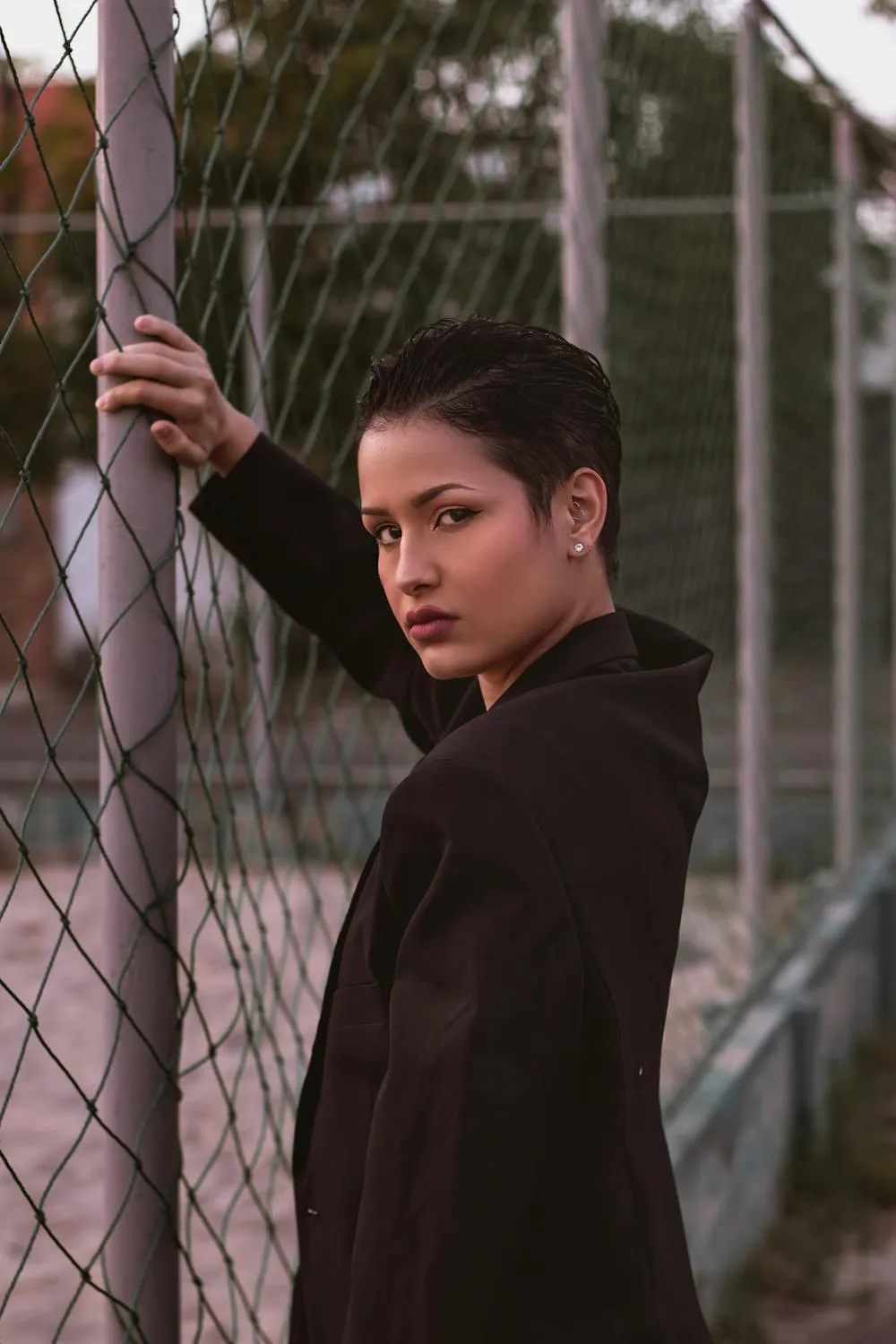 Confident Young Woman in Black Posing Behind a Chain Fence