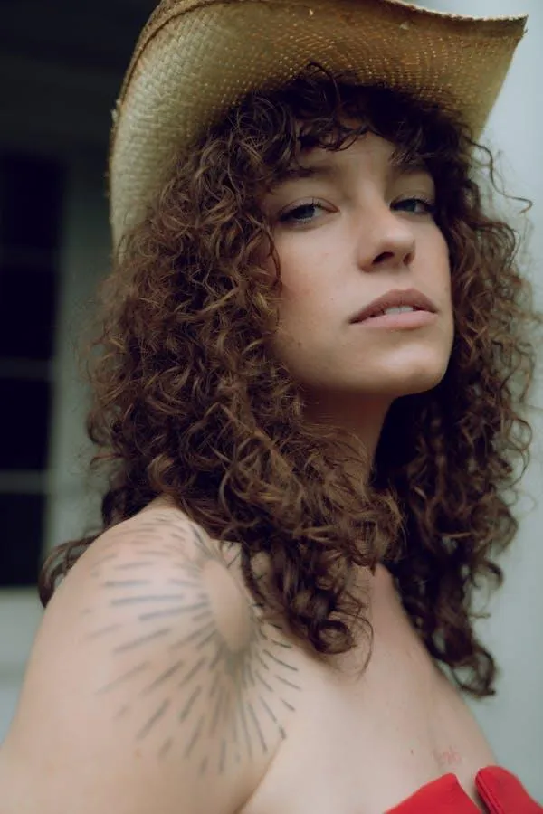 Curly Haired Woman in a Hat Looking Confidently At Camera