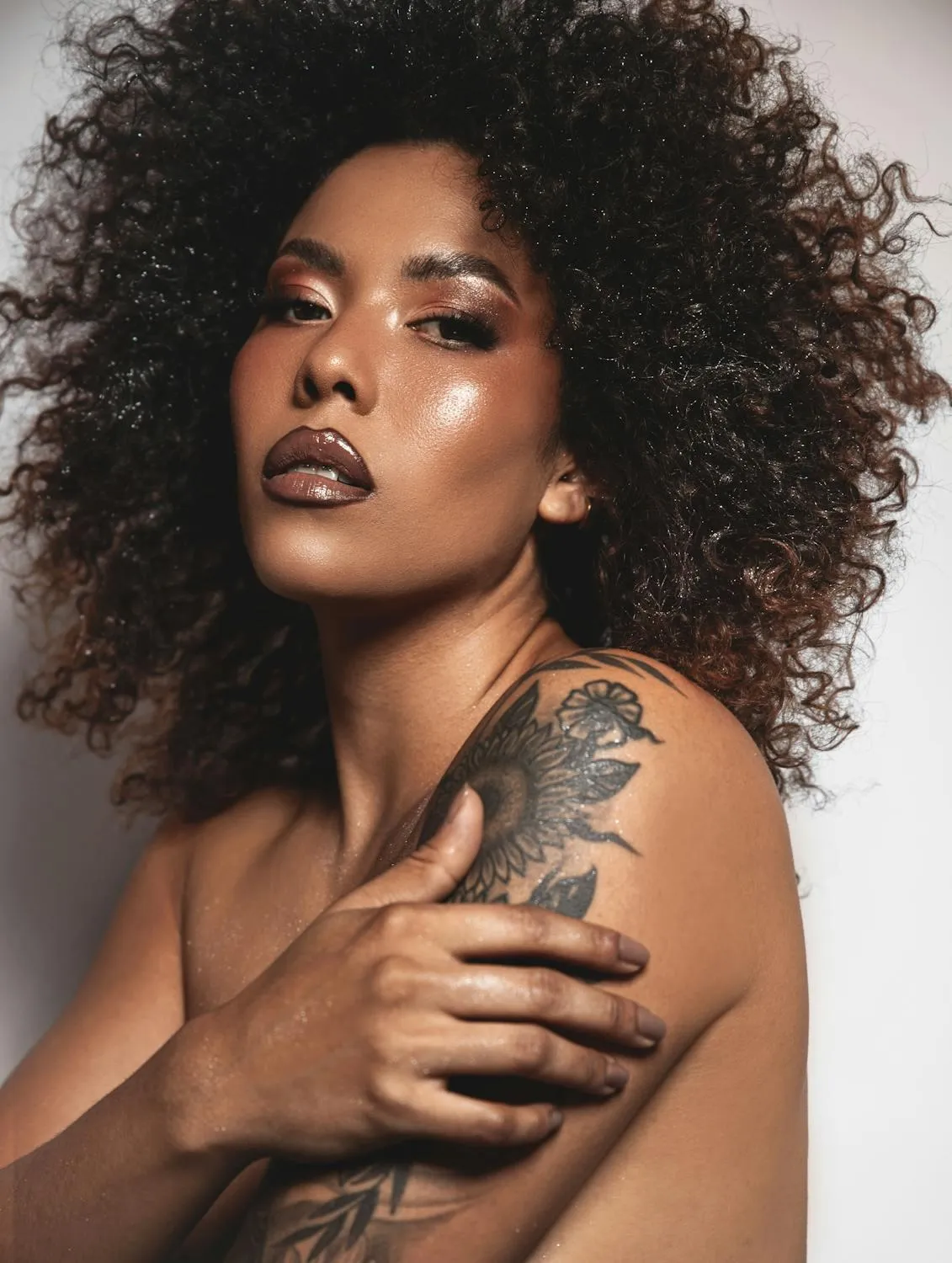 Curly Haired Woman with a Tattoo Embracing Herself on White