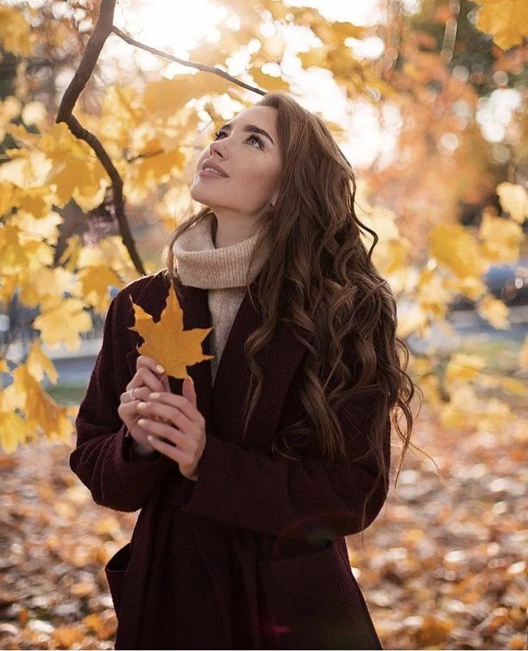 Cute Woman in a Dark Dress Holding Autumn Leaves in a Park