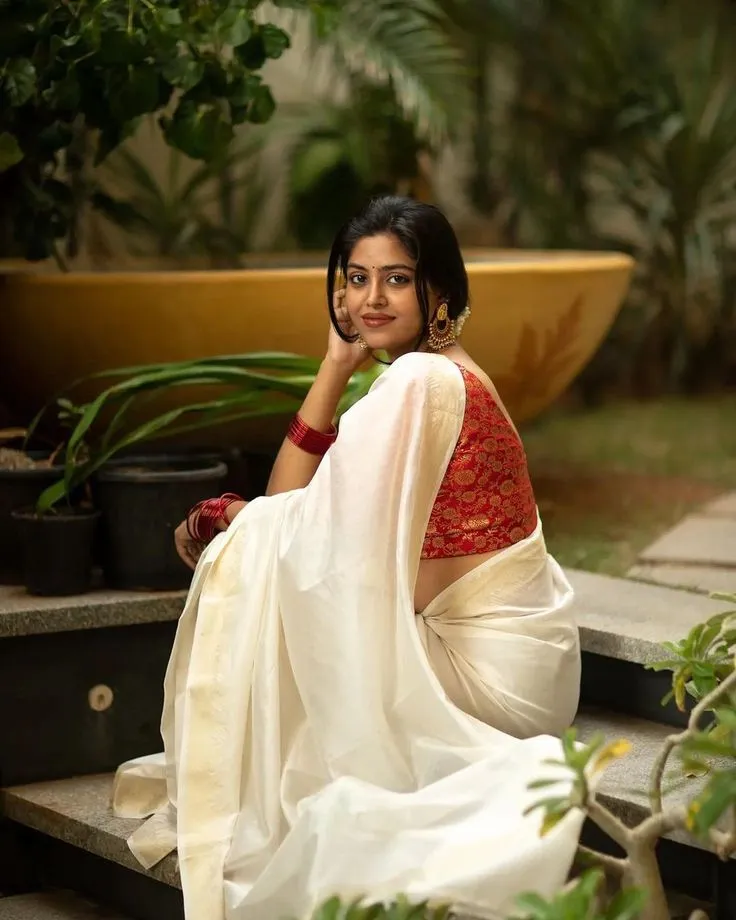 Devika Sanjay in a white saree sitting on the stairs image