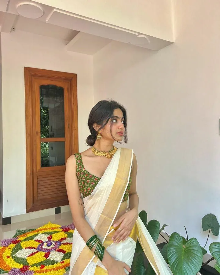 Devika Sanjay in Onam saree standing near the brown window