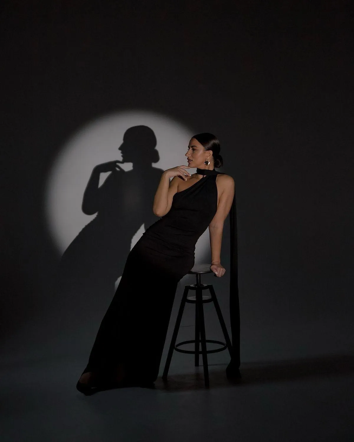 Elegant Woman Casting a Shadow While Posing on a Black Stool