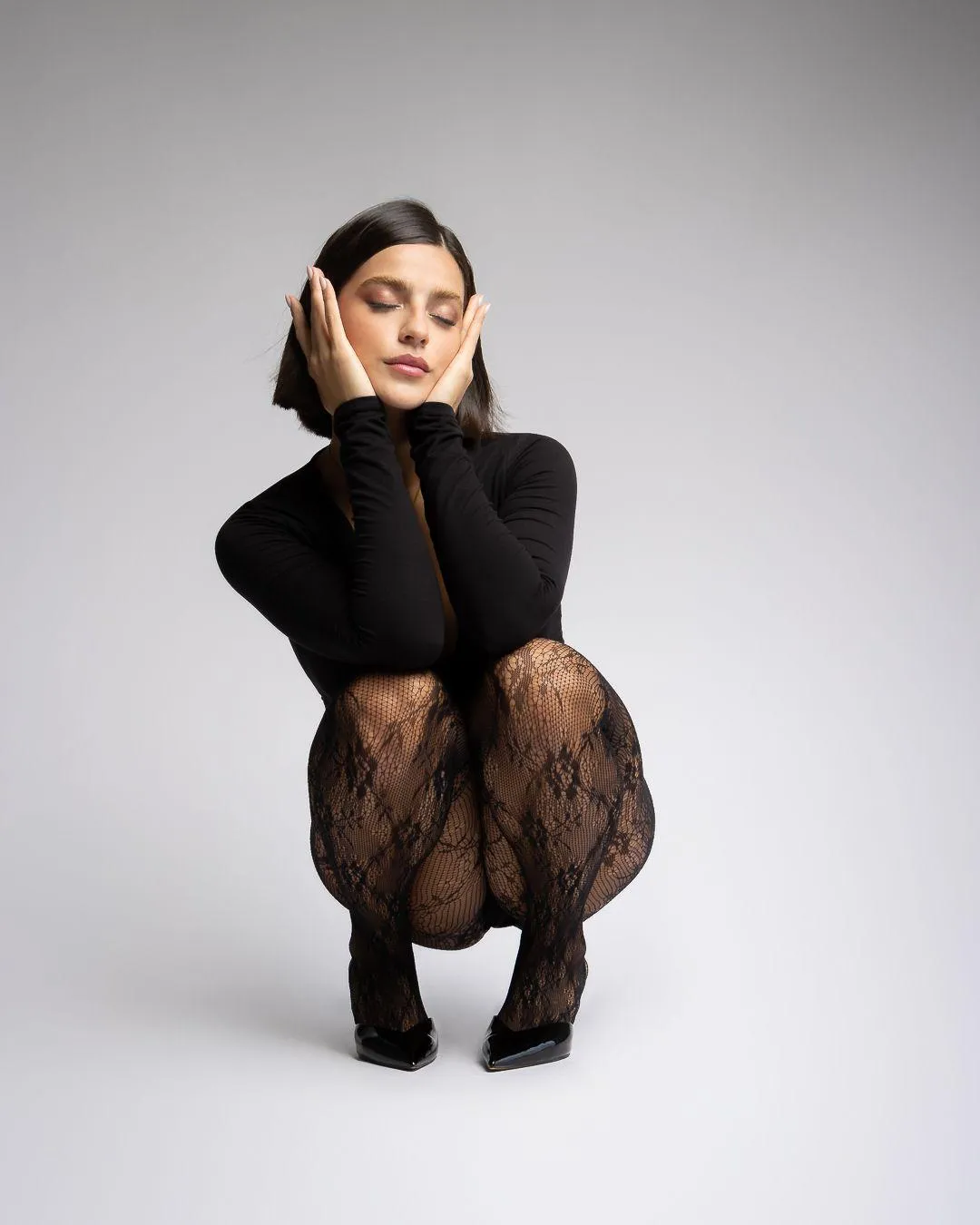 Fashion Model Sitting in a Black Outfit on a White Backdrop