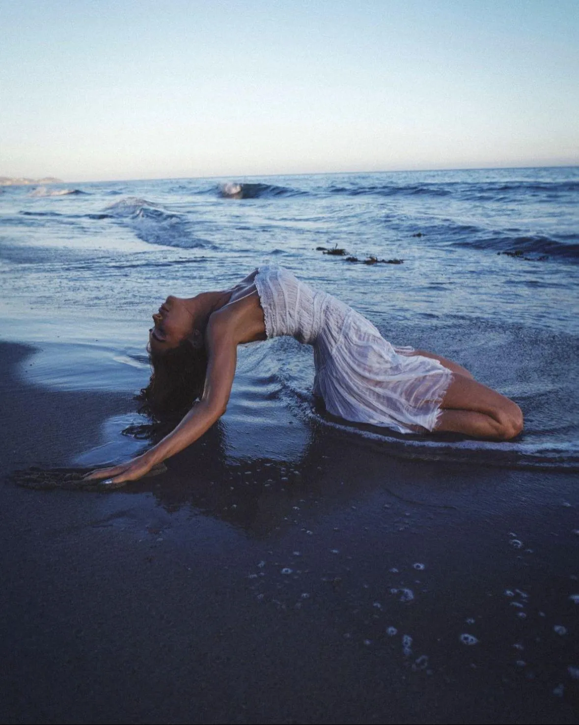 Female Model Lying on the Beach Shore in a Long White Dress