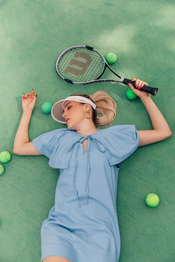 Girl in a Blue Dress Lying on Green Tennis Court with Racket