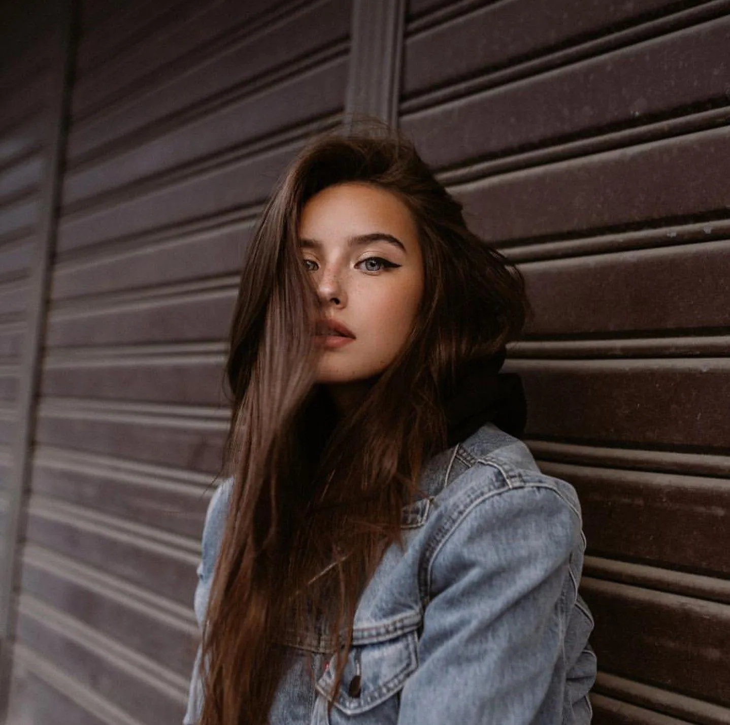 Girl in a Denim Jacket Standing Near Textured Brown Wall