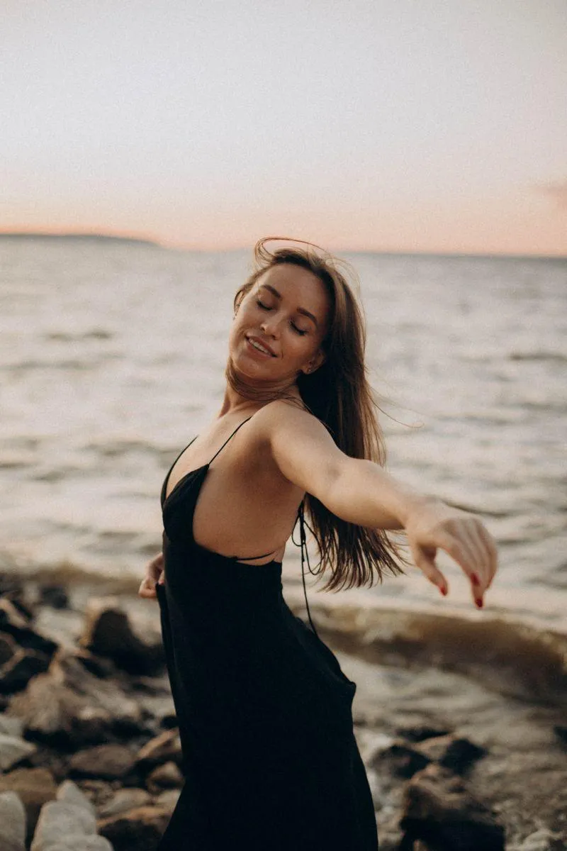 Happy Woman in a Black Swimsuit Standing by Ocean At Sunset