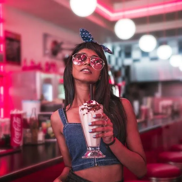 Happy Woman Enjoying a Milkshake in a Pink Retro Diner