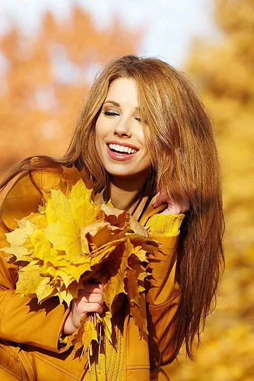 Happy Woman Holding Yellow Autumn Leaves and Smiling Widely