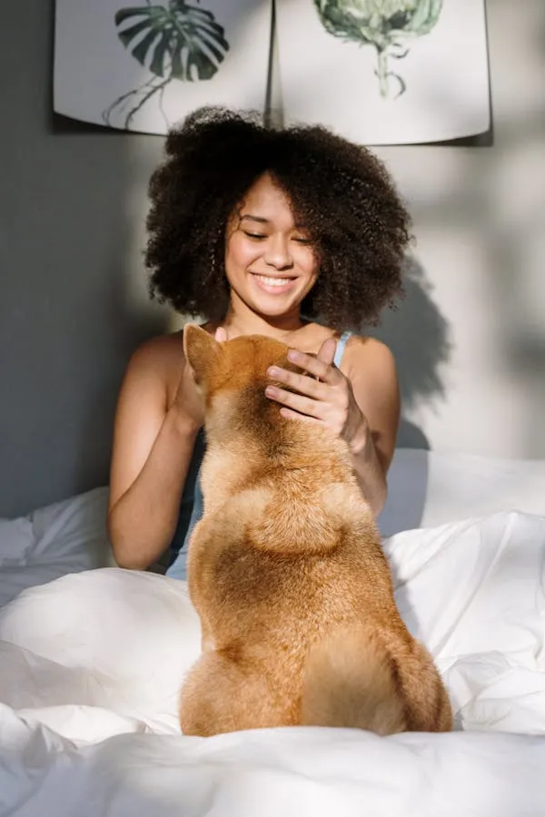 Happy Woman Playing with Dog While Sitting on White Bed