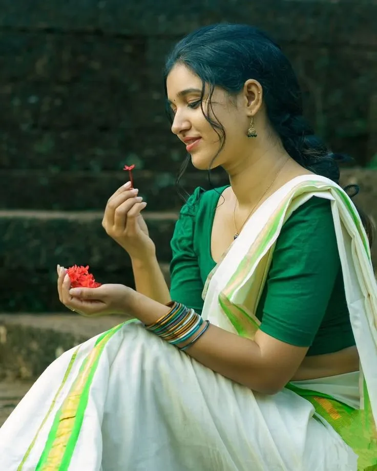 Haritha in an Onam saree holding a red flower HD wallpaper