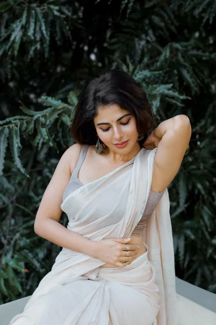 Iswarya Menon in a white saree standing near green leaves