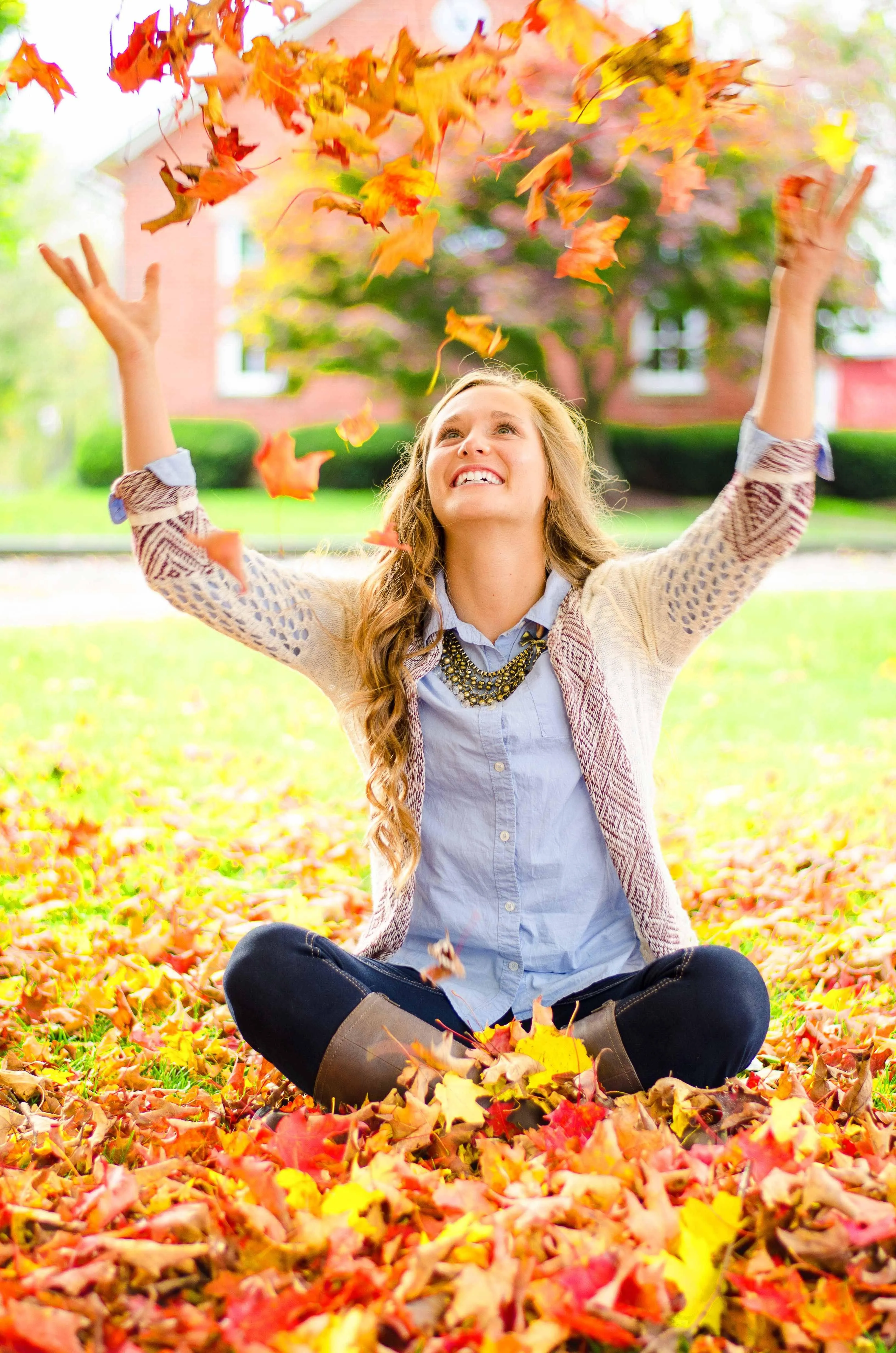Joyful Girl Sitting on Autumn Leaves with Arms Lifted High