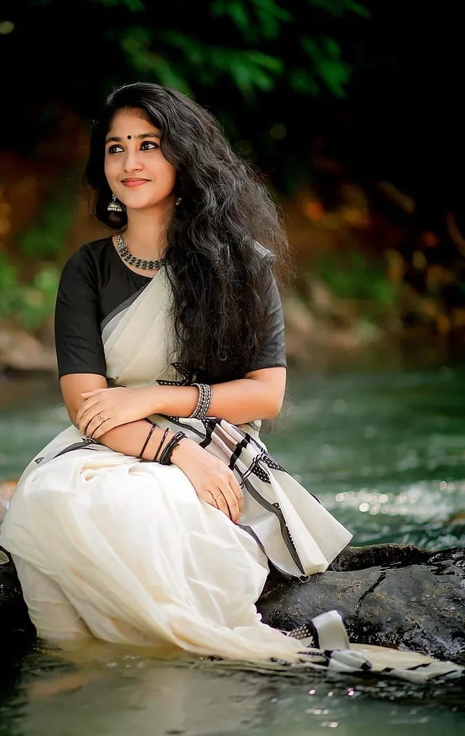 Kalyani Anil in a white and black saree sitting in the water