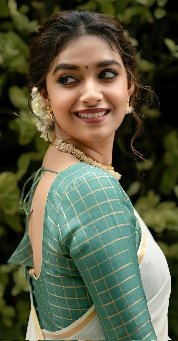 Keerthy Suresh in a side pose with a smile wearing a saree