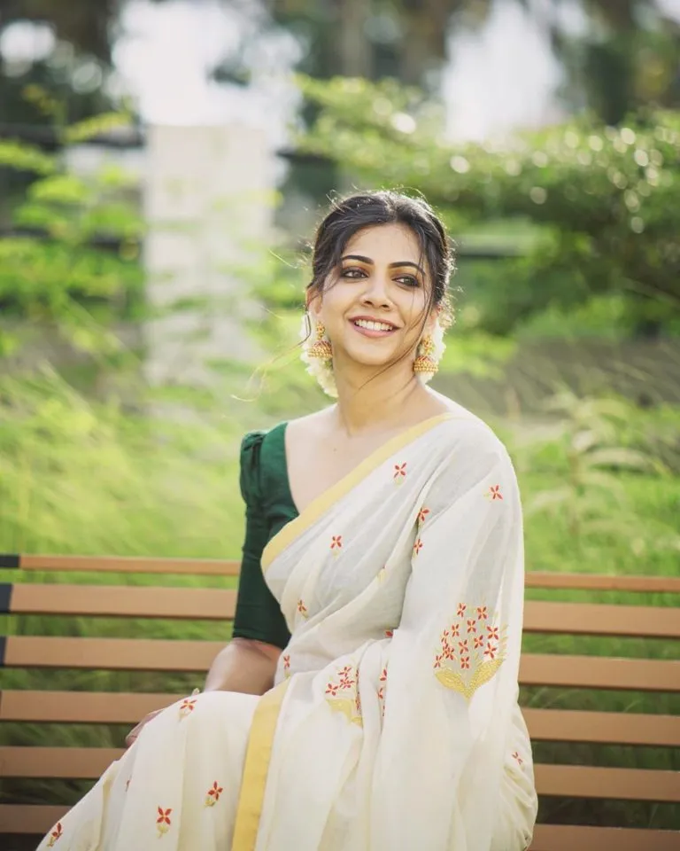 Madonna Sebastian in a Kasavu saree sitting on the bench