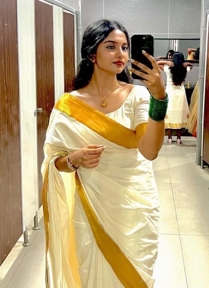 Mamitha Baiju in a kasavu saree holding a mobile phone