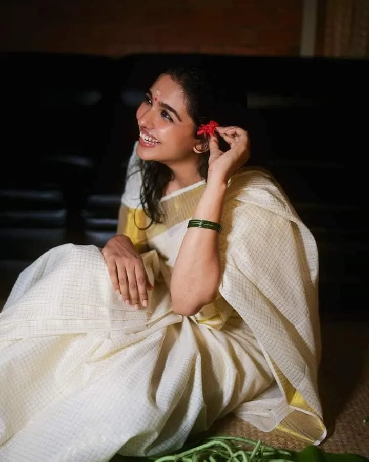 Mamitha Baiju sitting in an Onam saree with traditional pose