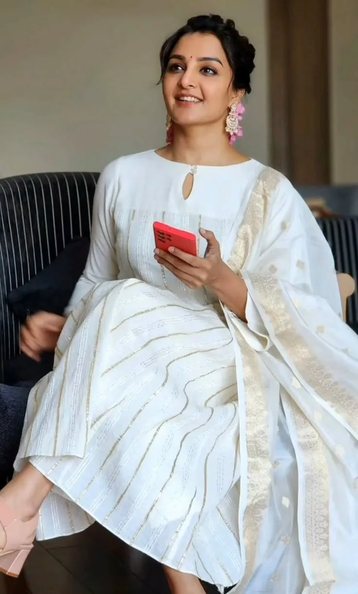 Manju Warrier in a white dress sitting on the black couch