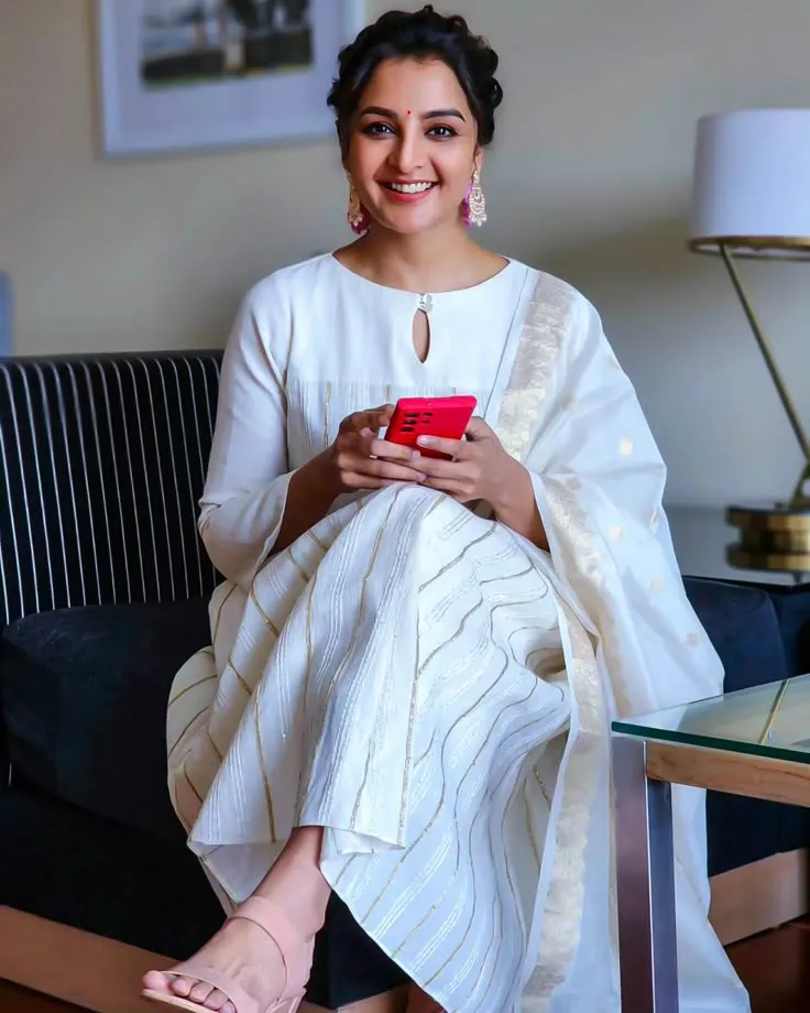Manju Warrier in a white outfit sitting with a red phone