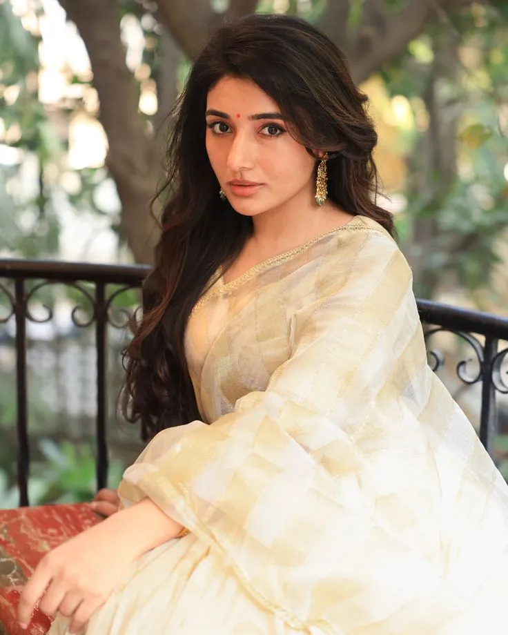 Mirna Menon in an Onam saree sitting near the black fence