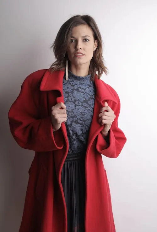 Modern Woman in Red Coat Posing Confidently Near White Wall