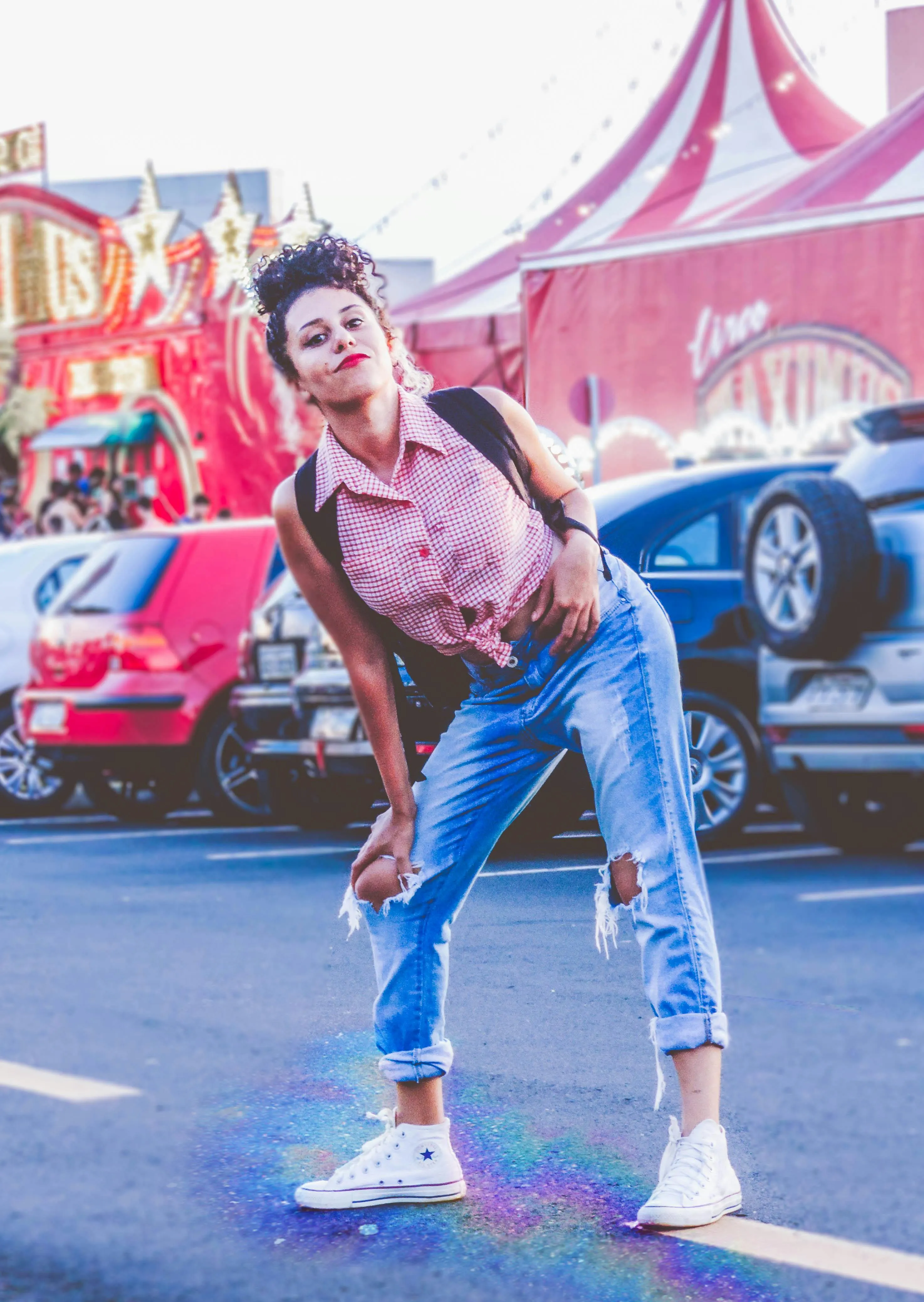 Playful Woman in Jeans Dancing Near Cars and a Circus Tent