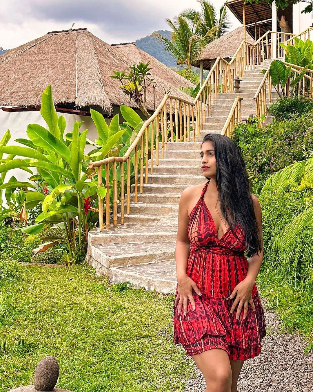 Pratika Sood in Red Dress Walking Near Lush Garden Path