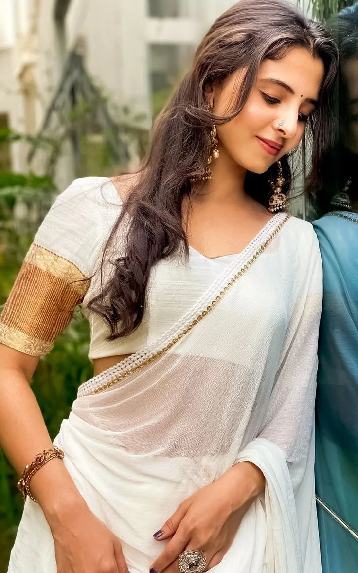 Preethi Asrani in a white saree leaning on the black car