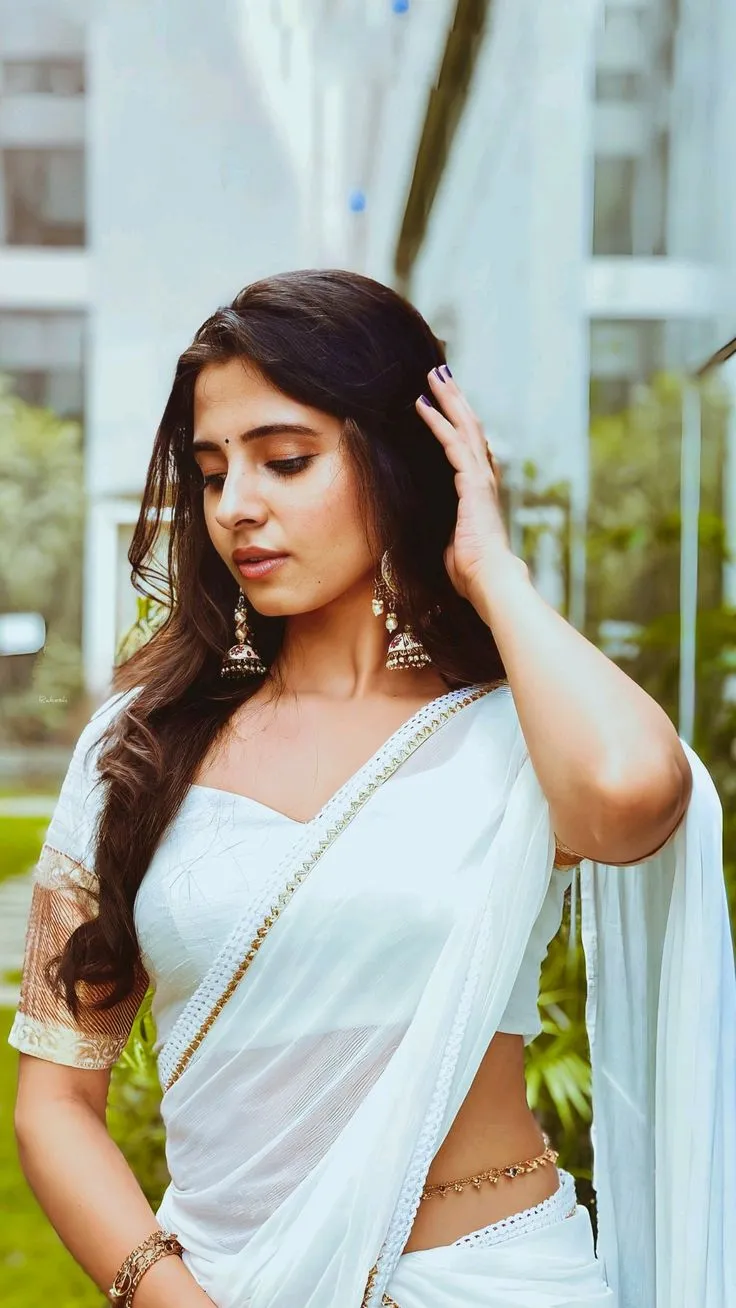 Preethi Asrani in a white saree with a building background