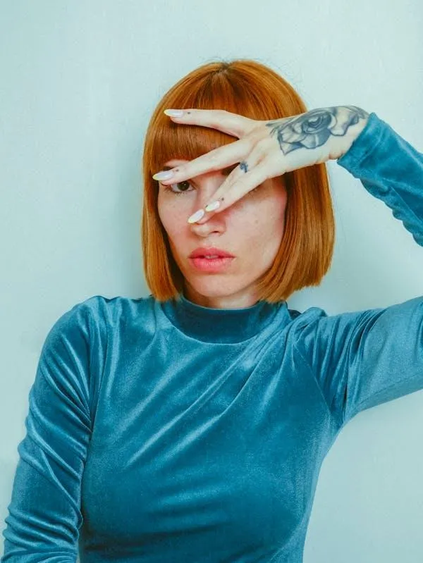 Red Haired Woman Covering Face with Hand in Teal Velvet Top