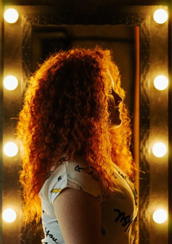Red Haired Woman Standing Near a Lit Mirror Backstage Scene